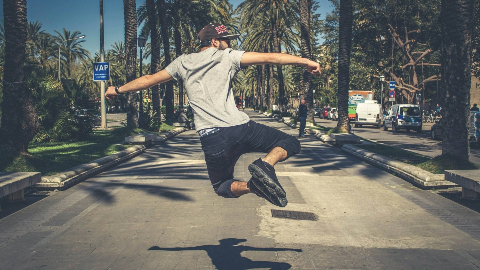 A person mid-jump on a sunlit street lined with palm trees, casting a long shadow