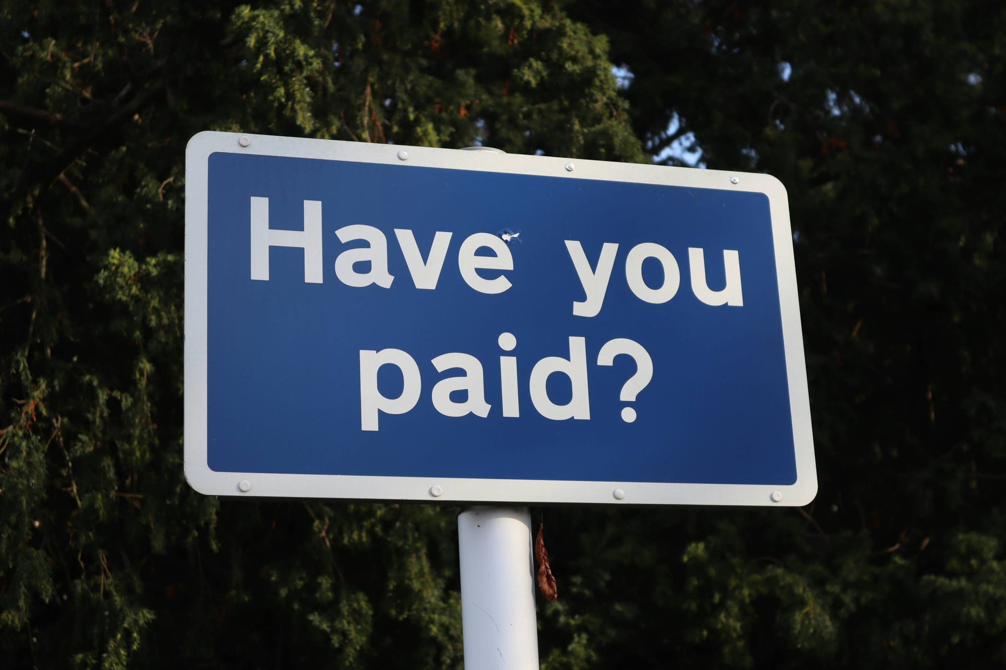 A blue sign on a wall reading Have You Paid