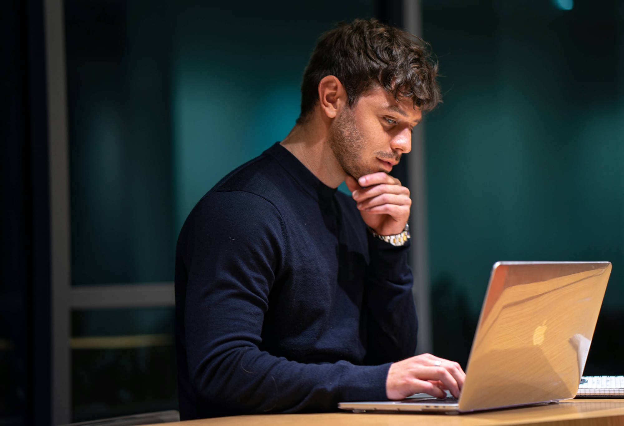 A person working alone at a laptop in a dark room