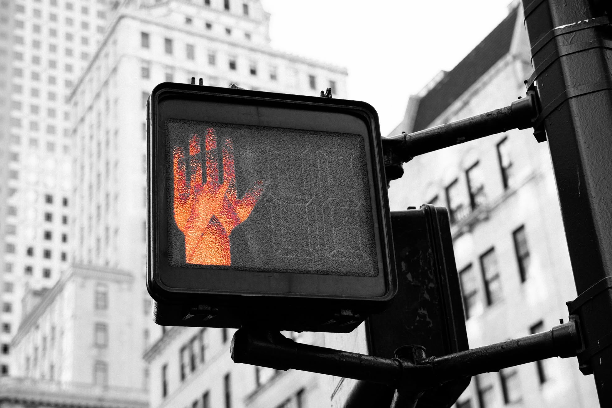 A pedestrian crossing signal showing the red stop hand, against a black and white city street