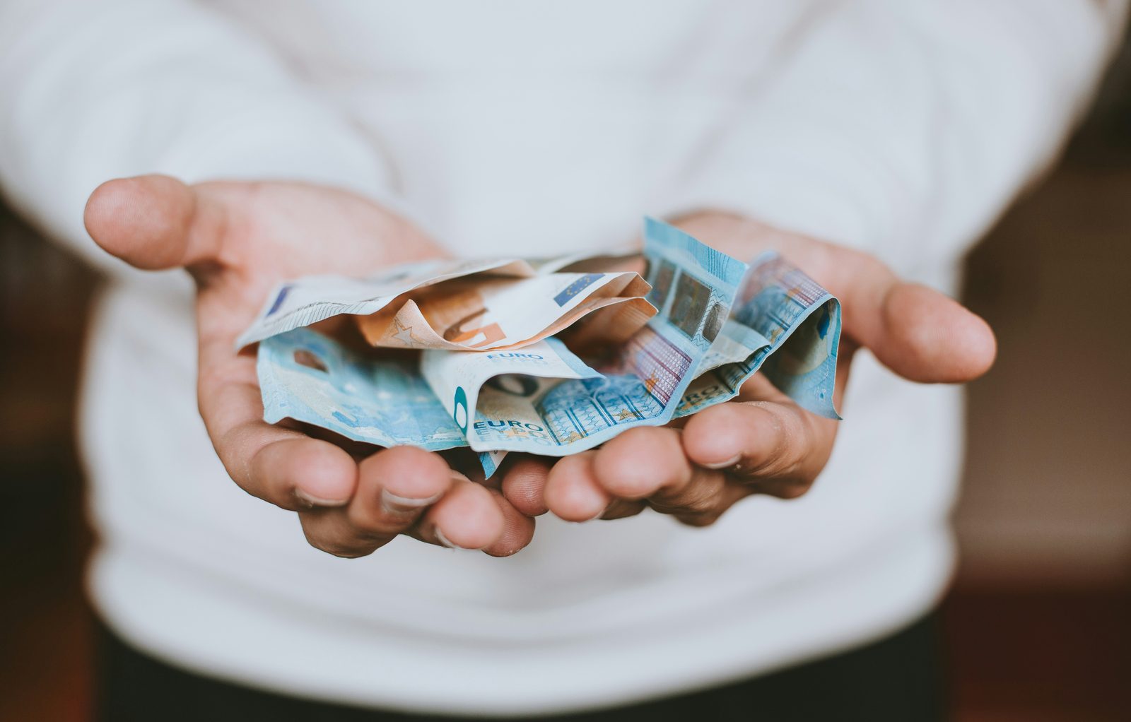 Two open hands holding a small stack of euro banknotes