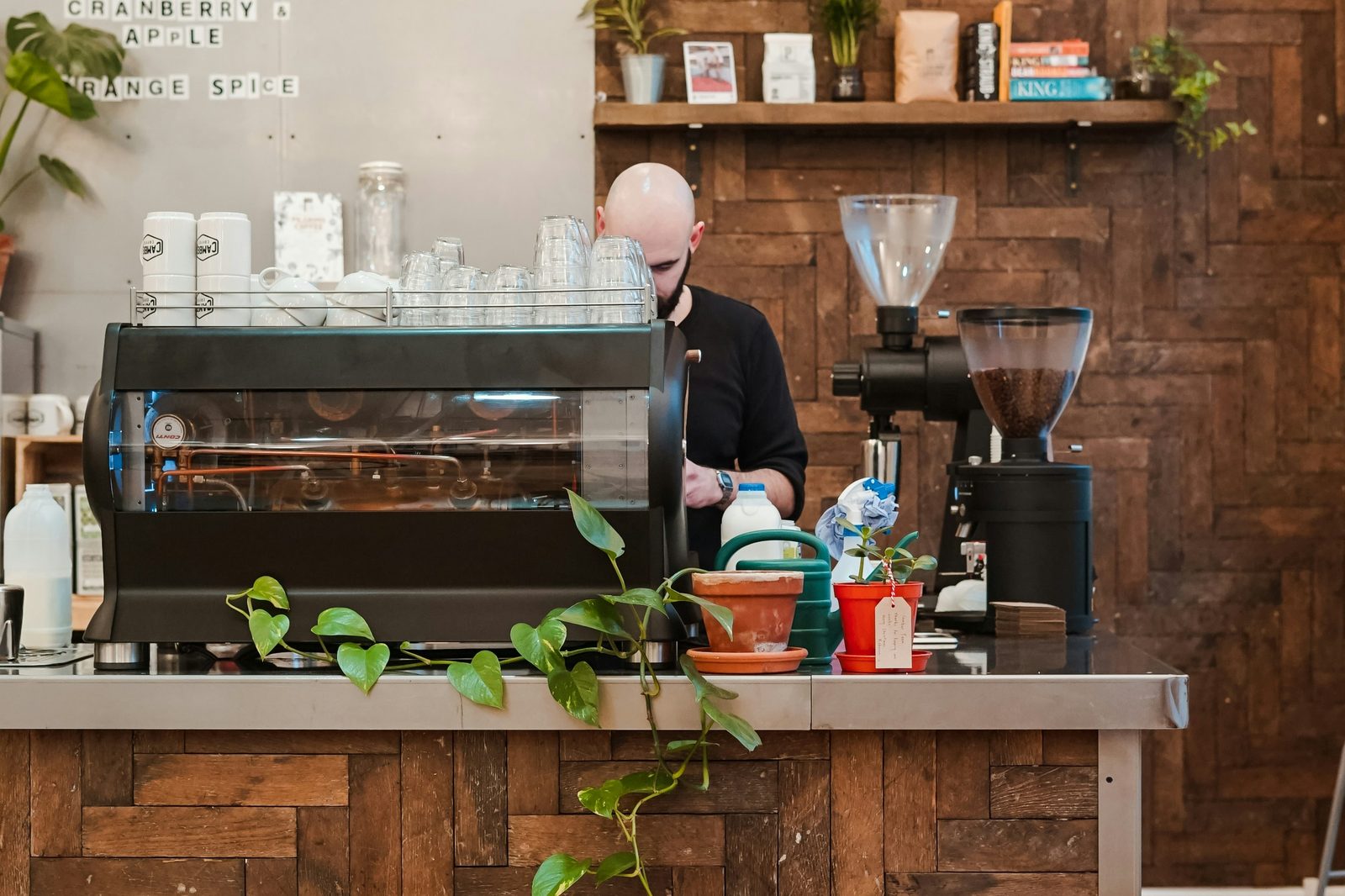 A barista working behind an espresso machine in a plant-filled coffee shop