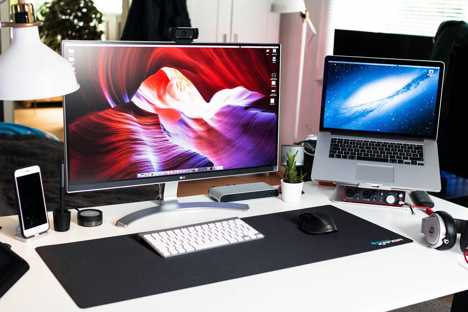 A desk with a large monitor showing a canyon wallpaper next to an open laptop