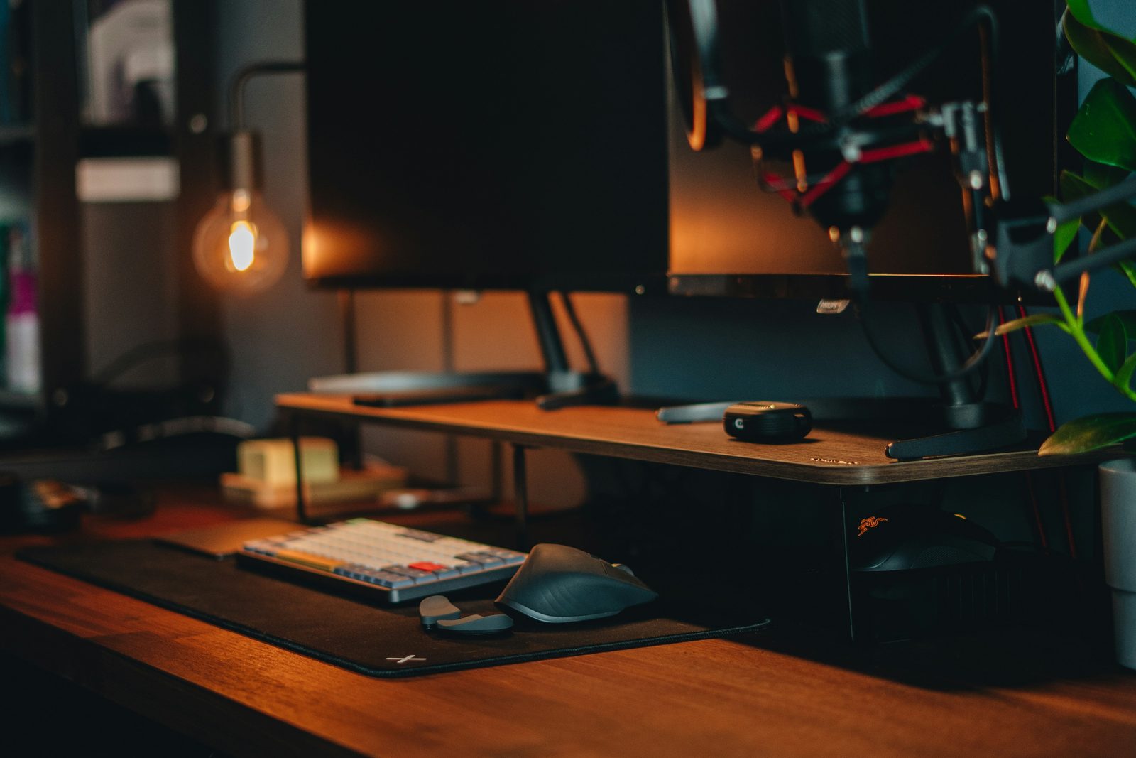 A dim desk with a microphone, a warm bulb lamp and a monitor in soft focus