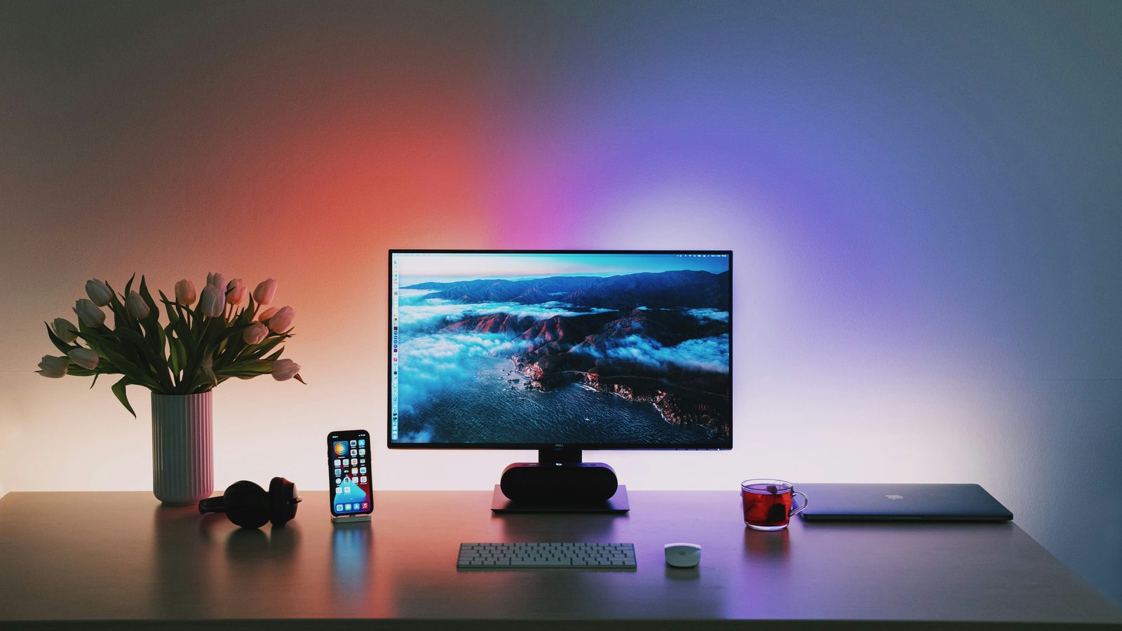 A desk with a monitor and phone lit by ambient RGB light spilling onto the wall
