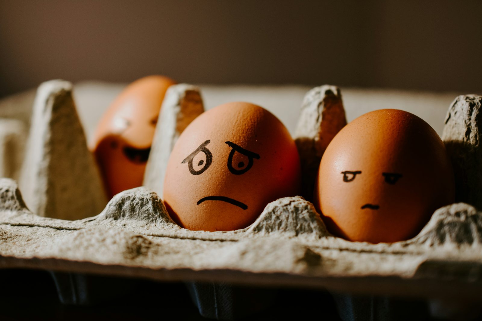 Three eggs in a carton with unhappy faces drawn on them in marker