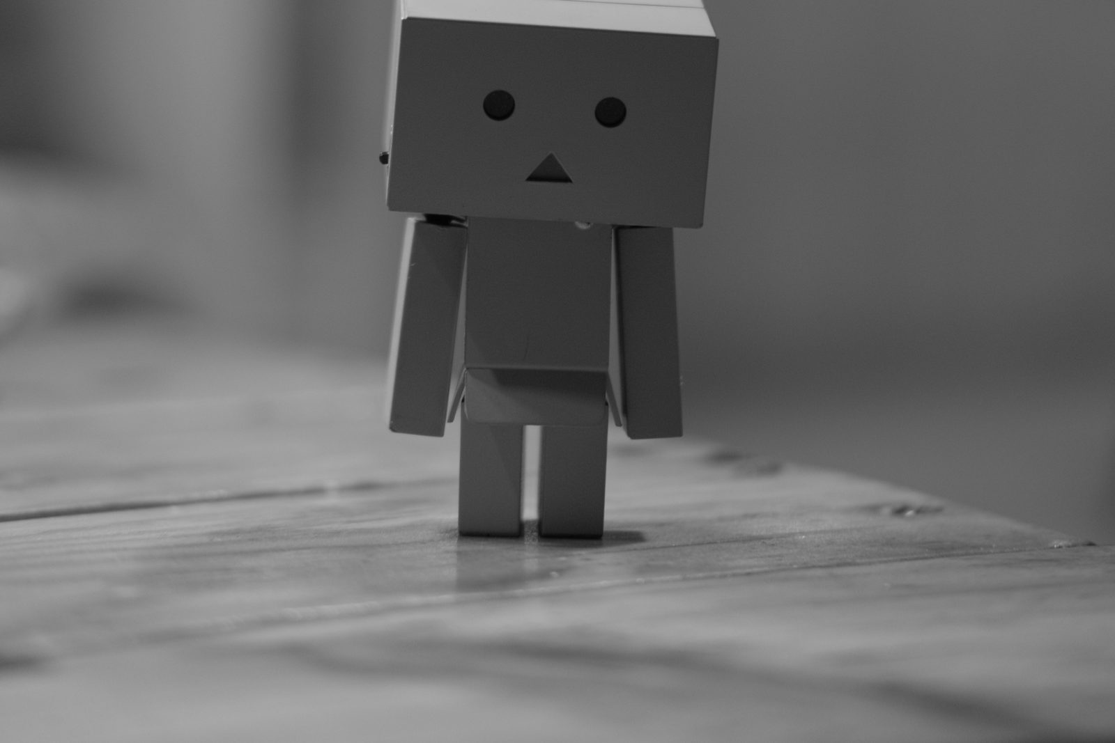 A small cardboard robot figure standing alone on a wooden table