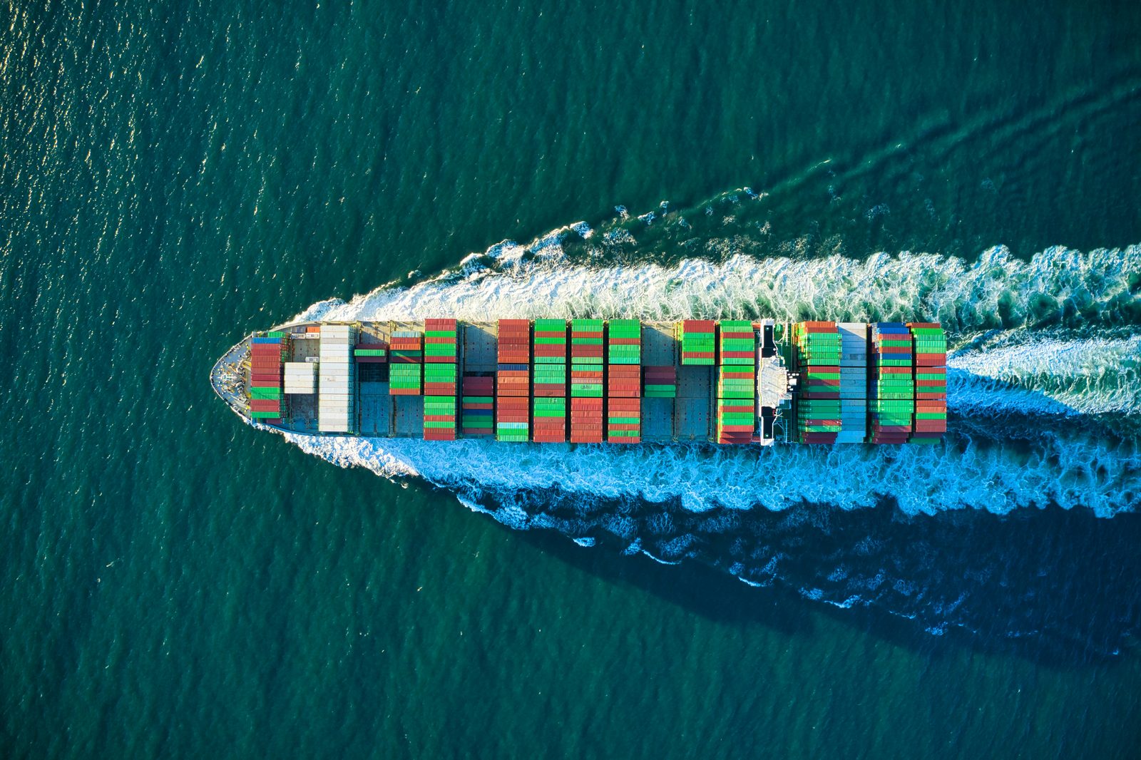 A container ship seen from above, cutting a wake through dark green water