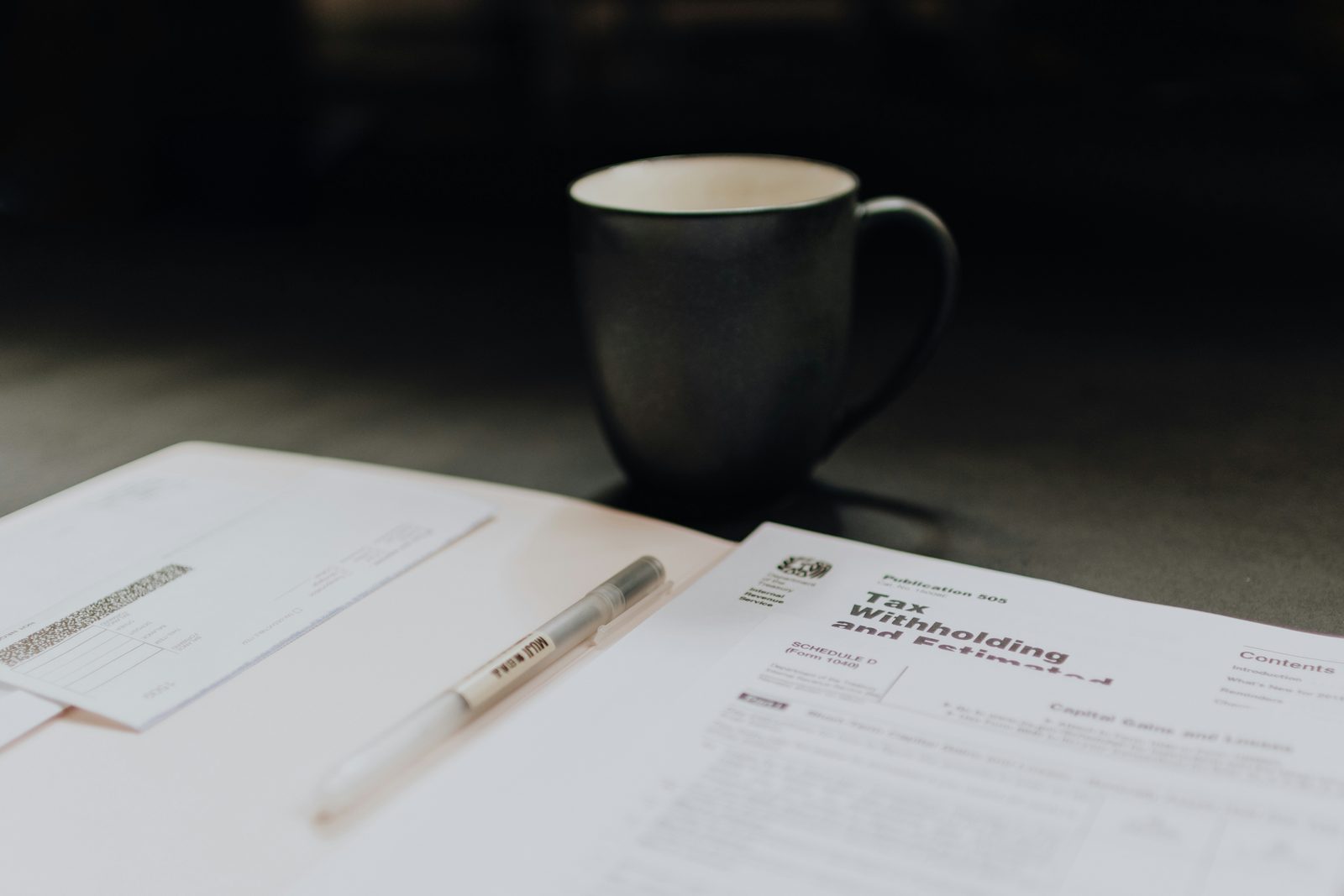 A tax form and a pen on a desk next to a dark coffee mug