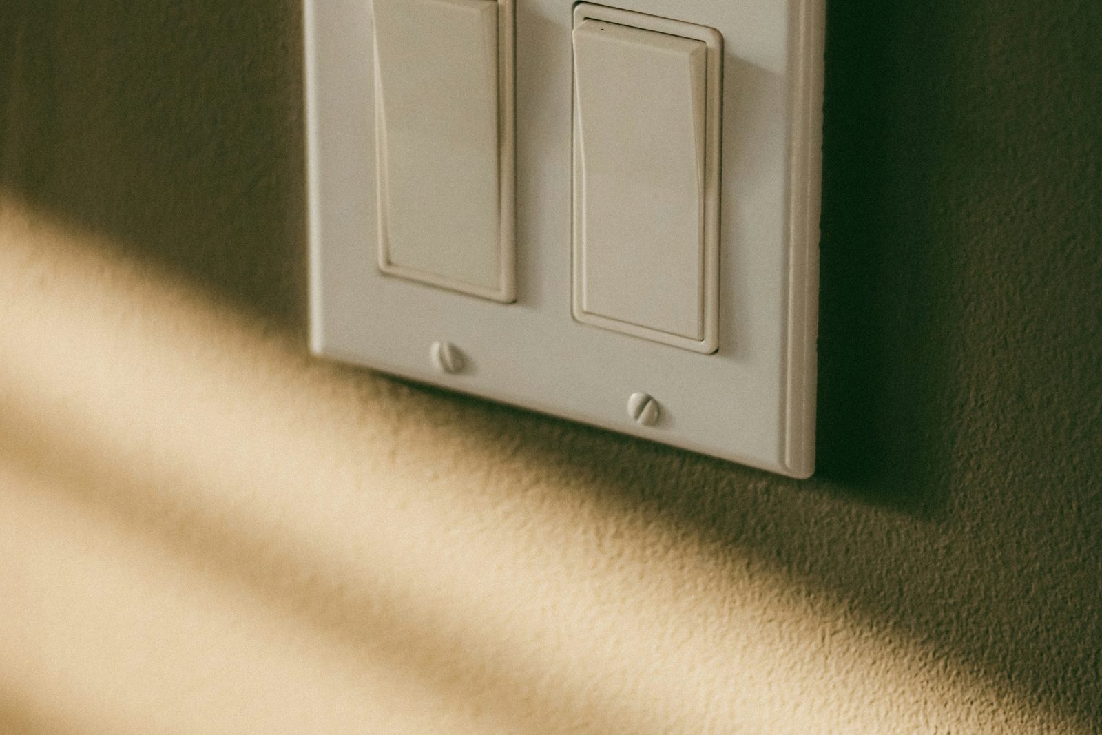A double light switch on a wall, low sun falling across it