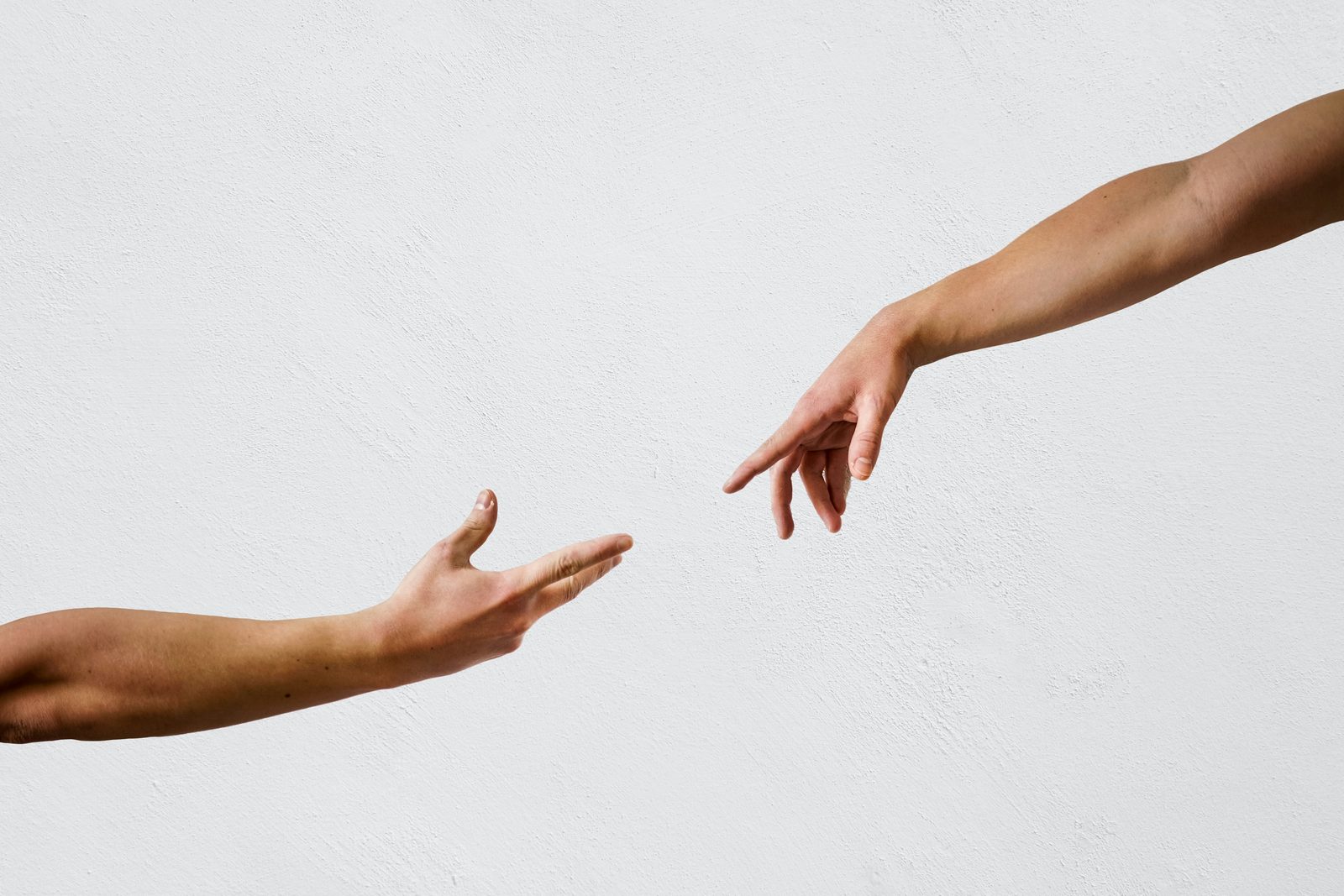 Two arms reaching toward each other against a plain white wall, fingertips not quite touching