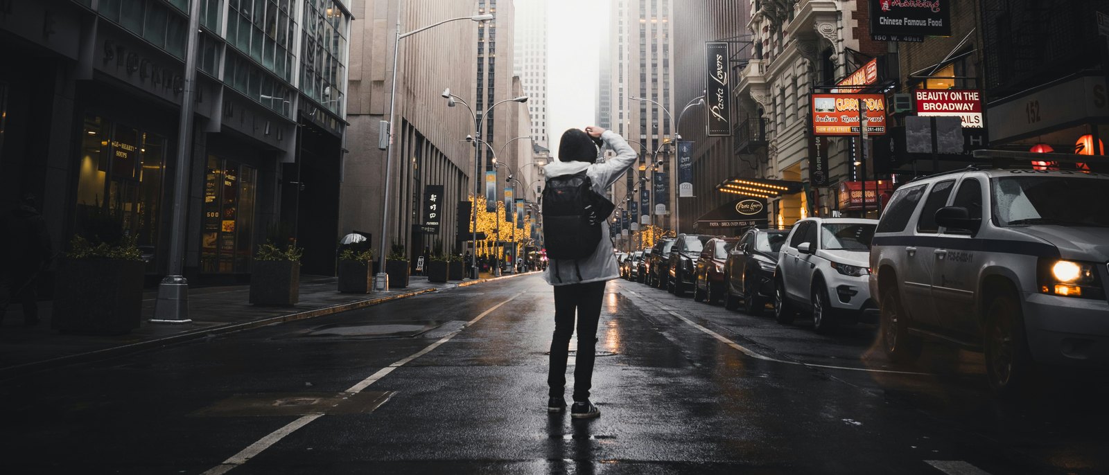 A person standing alone in the middle of a wet Manhattan street, the buildings on both sides running up into bright fog that swallows the far end