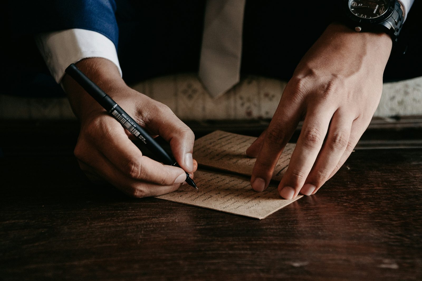 Close-up of hands in a suit signing a handwritten note with a black pen on a dark wooden table