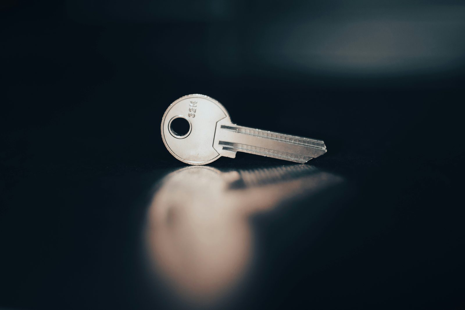 A single silver key lying on a dark reflective surface, lit from the side