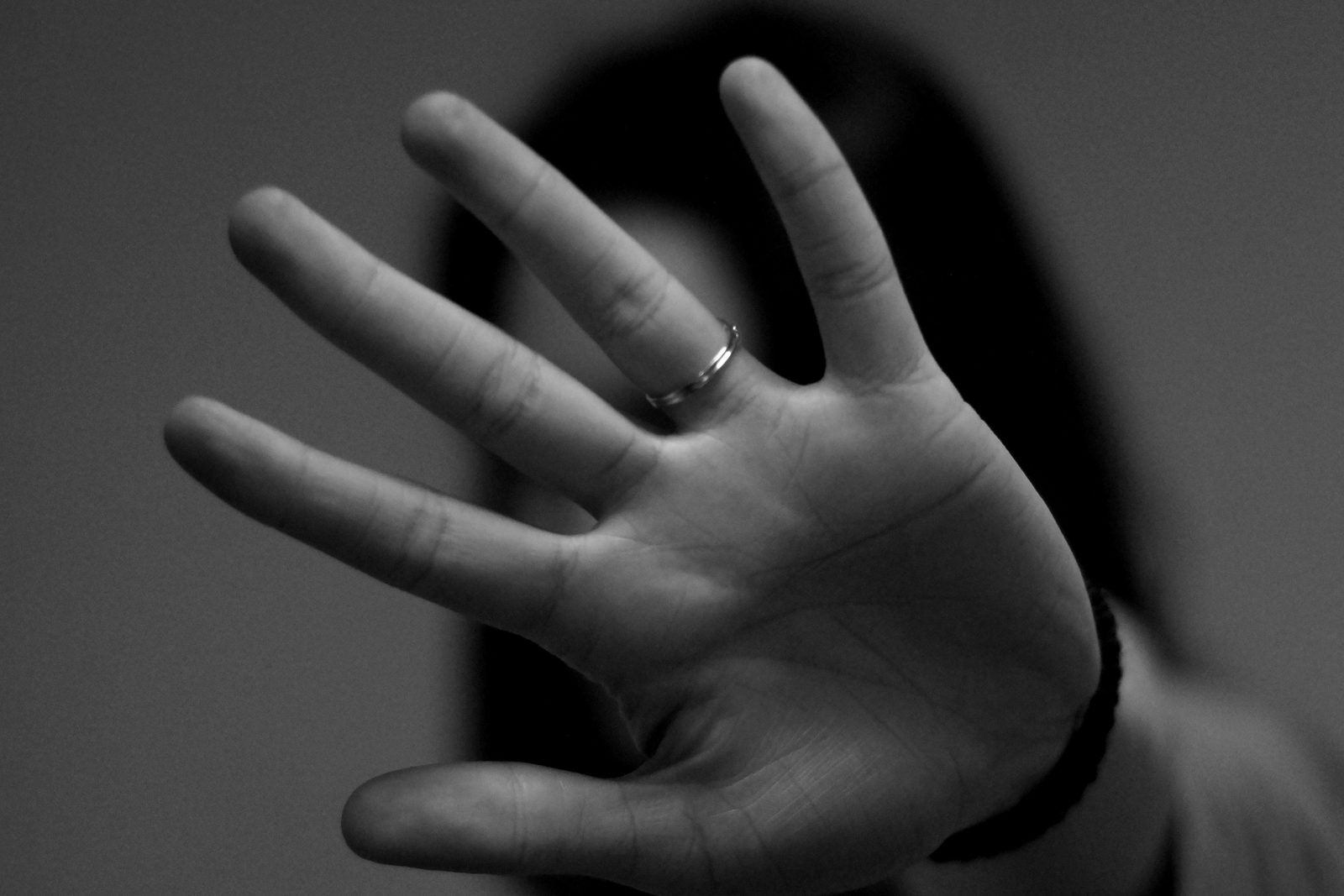 A black and white photo of a person holding an open palm towards the camera, hiding their face behind the hand