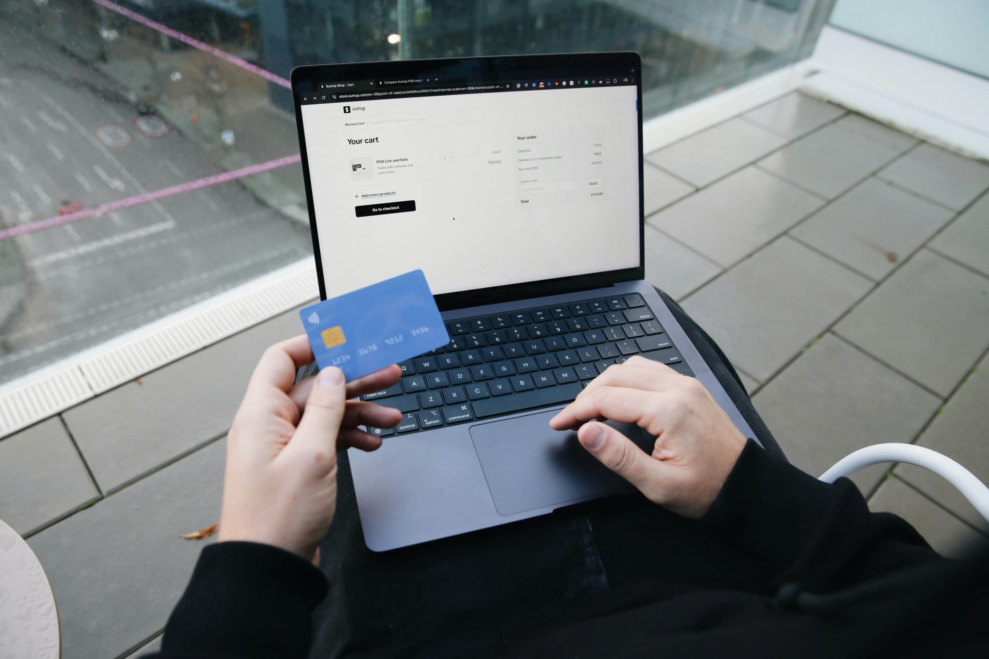 Someone holding a bank card over a laptop keyboard while a checkout page waits on screen