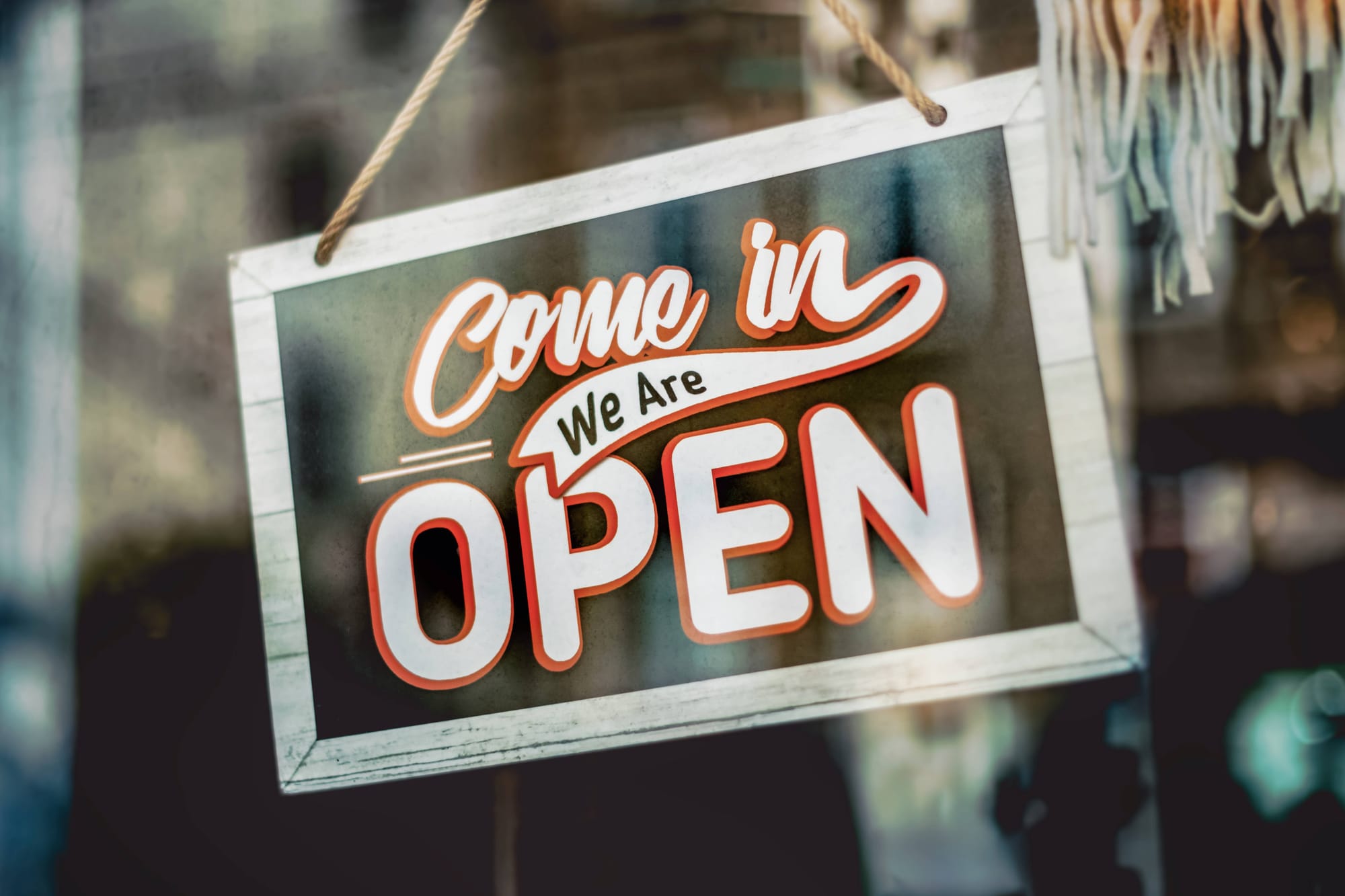 A hand-lettered shop sign in a window reading Come in, We Are Open